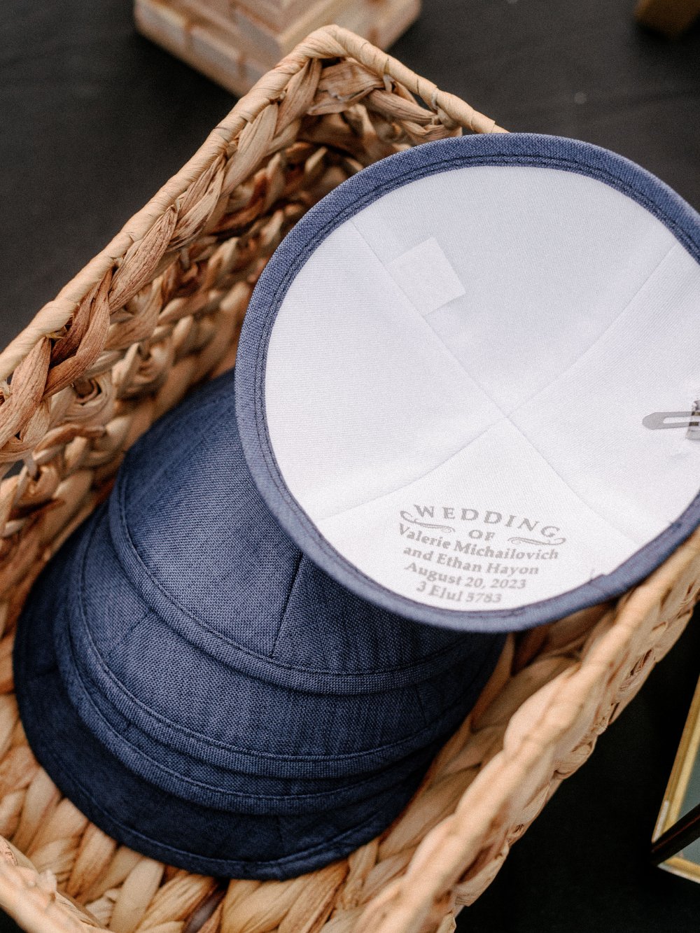 Wedding detail photos featuring personalized kippahs displayed in a woven basket for wedding guests.