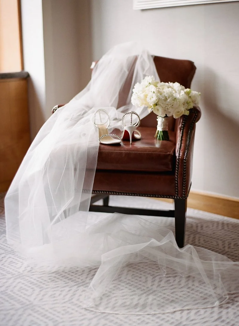  bridal shoes, bouquet, and veil sitting on top of a brown chair 