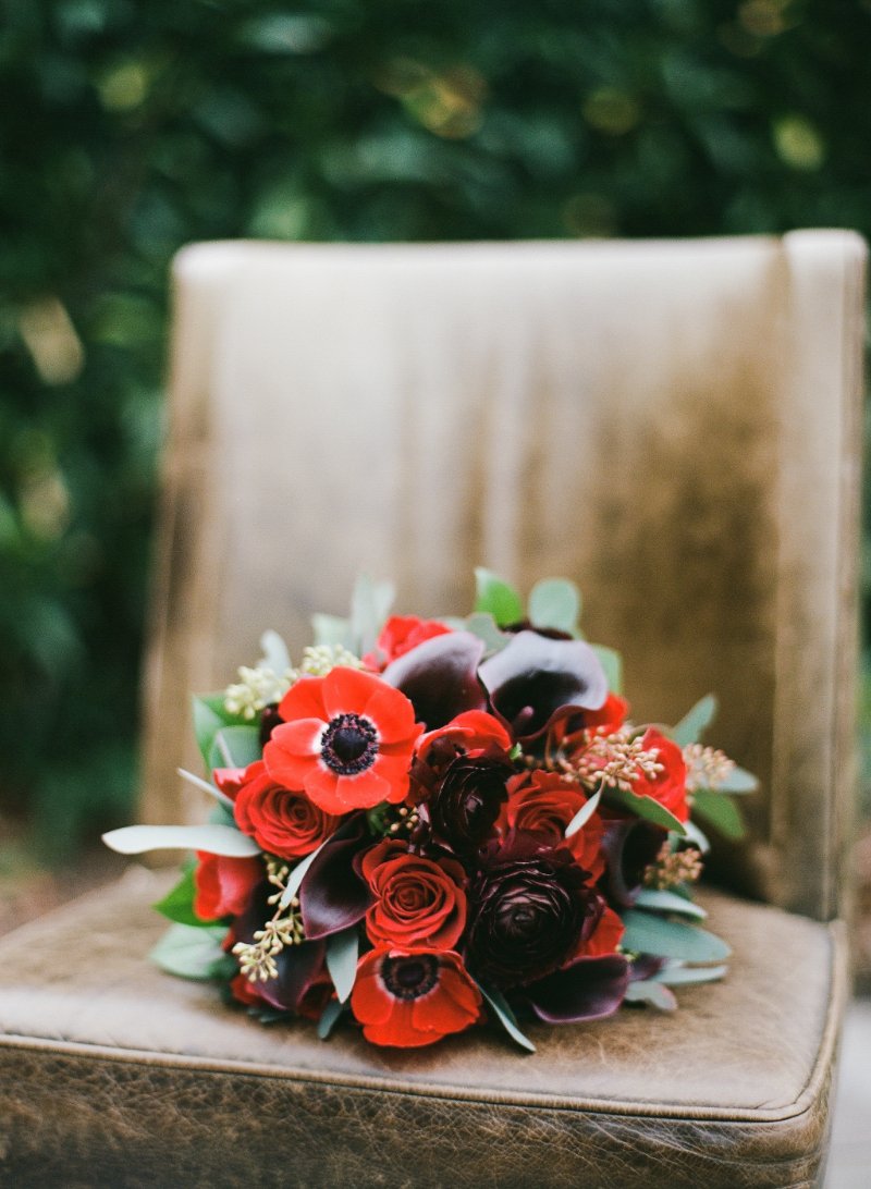  red and black bridal bouquet sitting on a brown chair outside 