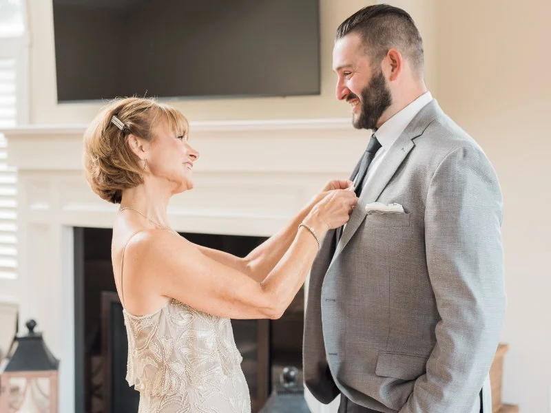 grooms mother pins his boutonniere to his lapel during getting ready wedding photography  