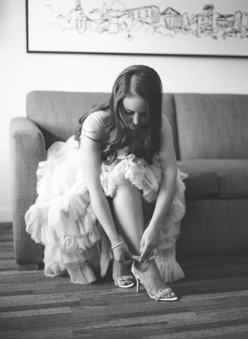  black and white photo of a bride sitting on a couch adjusting her heel strap  