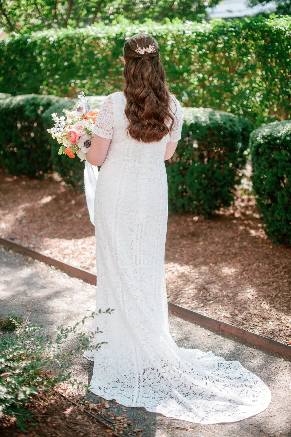  A bride in lace with flowing waves and a soft bouquet stands in serene garden light—an elegant moment at a  luxurious small intimate wedding .   