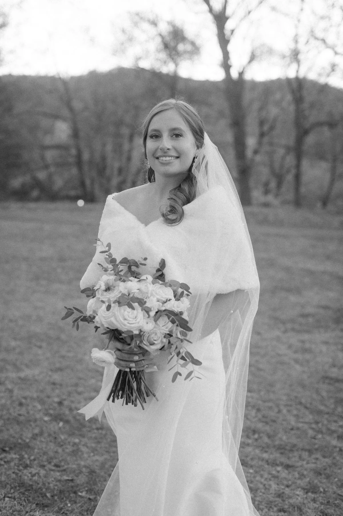  A bride in a cozy wrap holds soft pastel florals outdoors, showcasing elegant  winter wedding ideas  with romantic blooms, a warm shawl, and a timeless, serene seasonal vibe. 