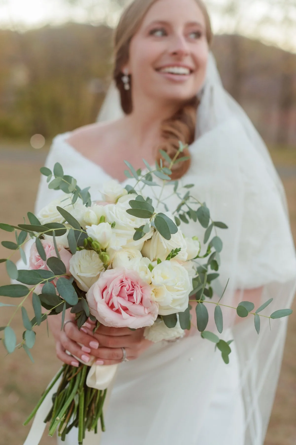  A bride in a cozy wrap holds soft pastel florals outdoors, showcasing elegant  winter wedding ideas  with romantic blooms, a warm shawl, and a timeless, serene seasonal vibe. 
