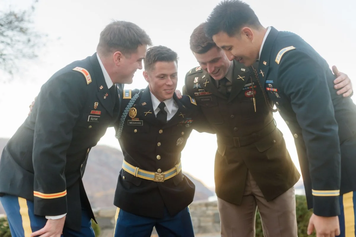  Four uniformed military officers huddle together outdoors, smiling and leaning in with a backdrop of soft, natural light. | intimate wedding photo timeline 