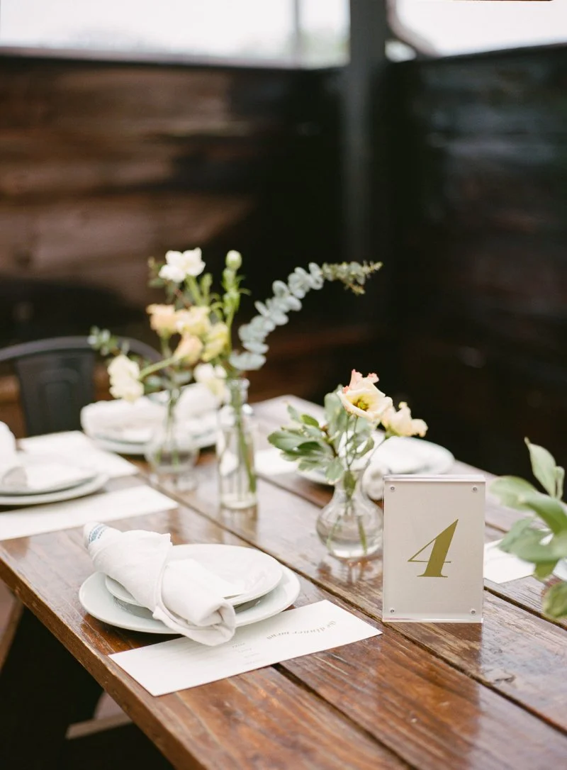  Minimal reception table styling with white plates, folded napkins, and simple florals at a rooftop wedding reception. 