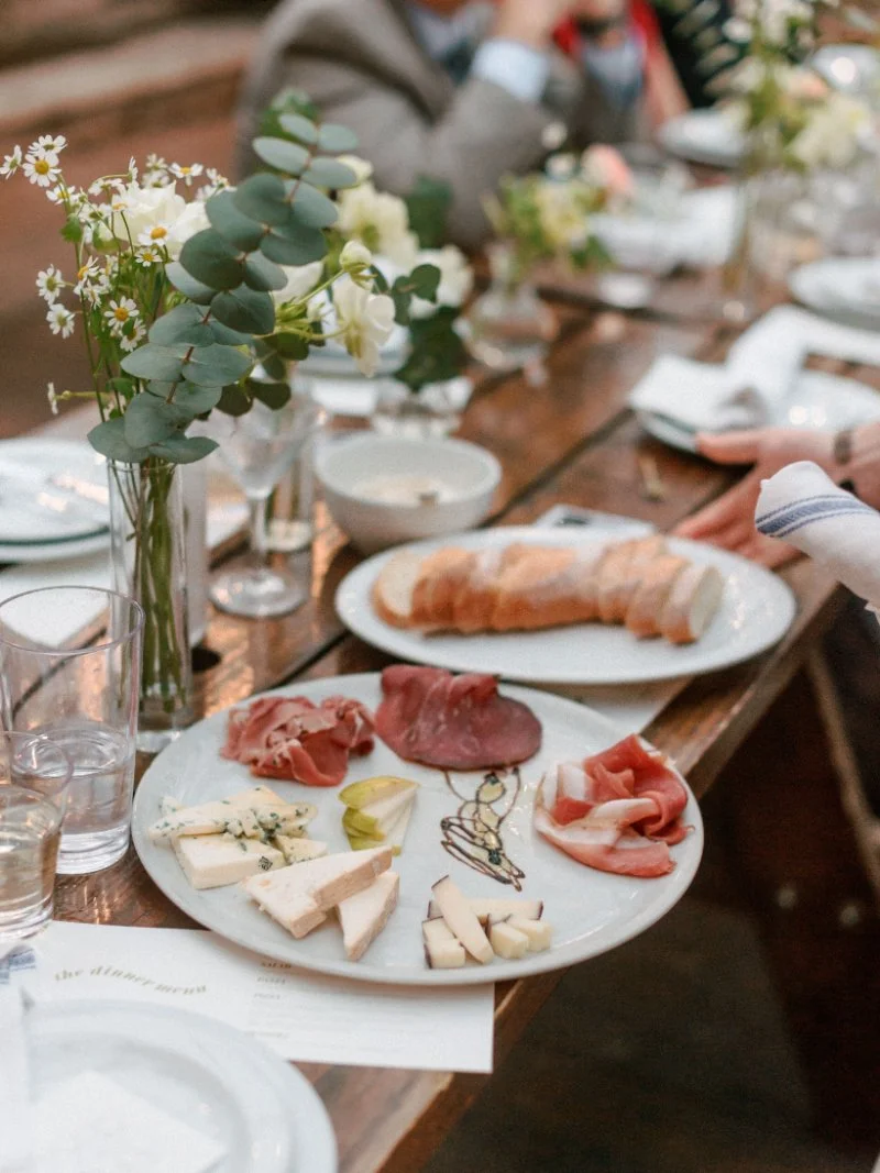  Charcuterie plates, croissants, candles, and florals styled across a long reception table during an intimate rooftop wedding. 