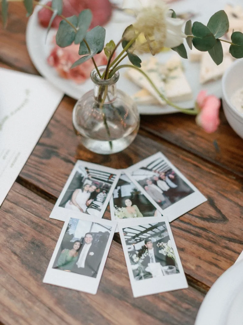  Instant film photos scattered across a reception table beside florals and dinner details after a rooftop wedding celebration. 