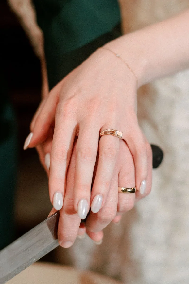  Close-up of wedding rings and manicured hands during the couple’s cake cutting moment at their rooftop wedding reception. 