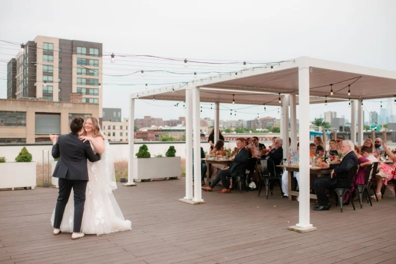  Guests watch the couple’s first dance during a rooftop wedding in Jersey City beneath string lights and an open-air reception space. 