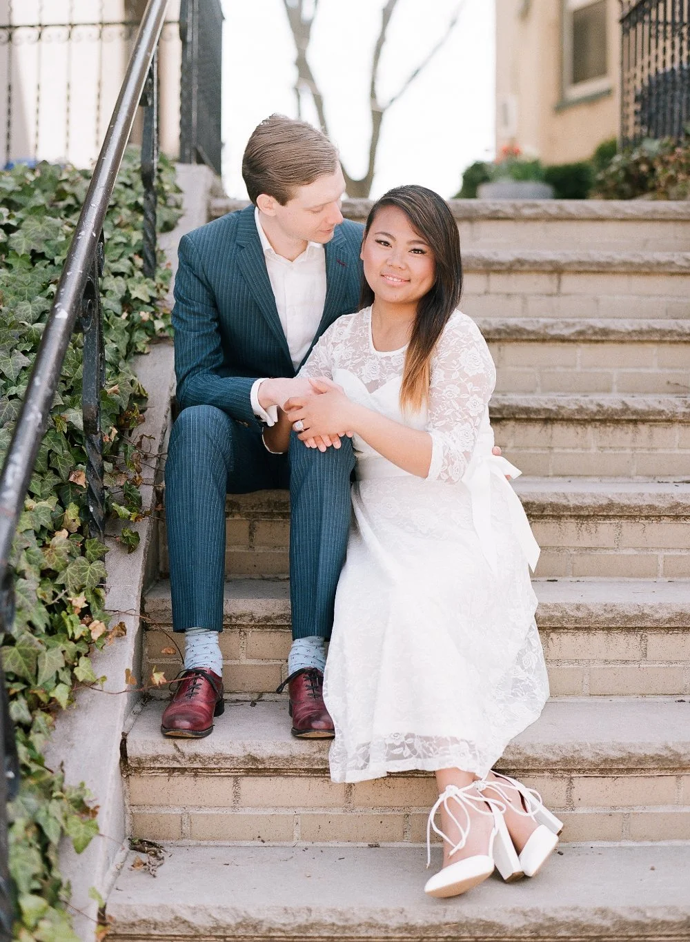  Couple sitting on stone steps in soft neutral outfits for timeless engagement photo outfit inspiration. 