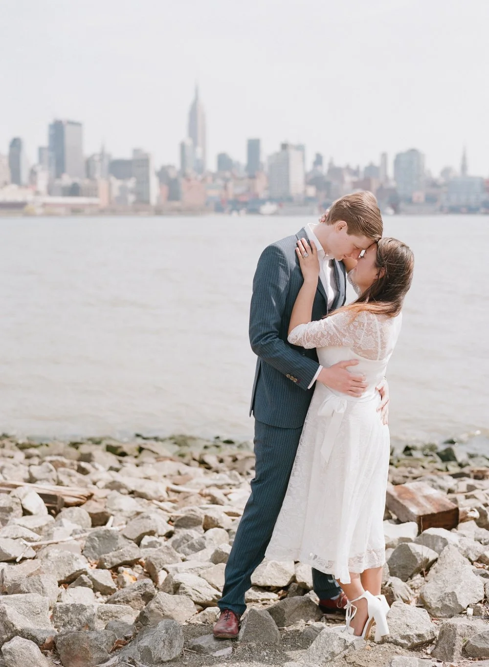  Couple kissing by the waterfront in soft, timeless outfits perfect for engagement photo inspiration. 
