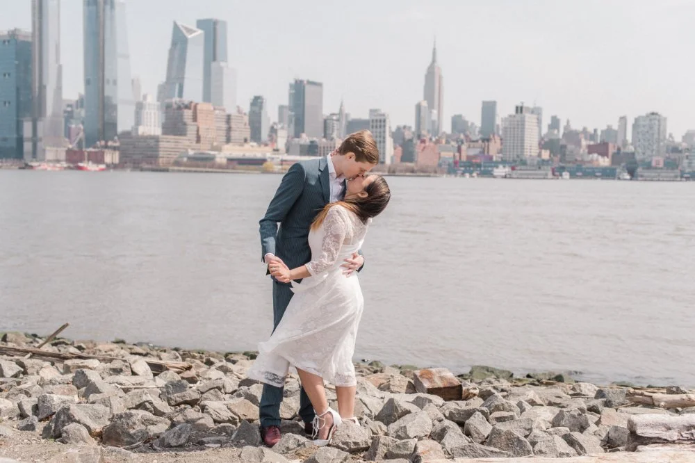  Waterfront couple embracing with skyline views and timeless what to wear for engagement photos inspiration. 