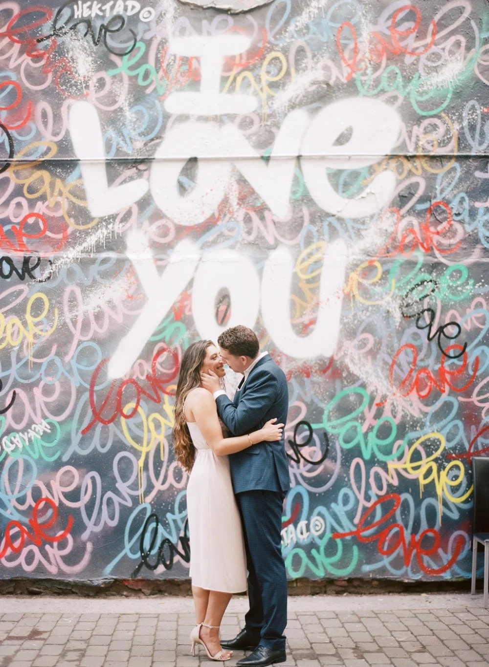  Couple embracing in front of colorful love mural with playful what to wear for engagement photos inspiration. 