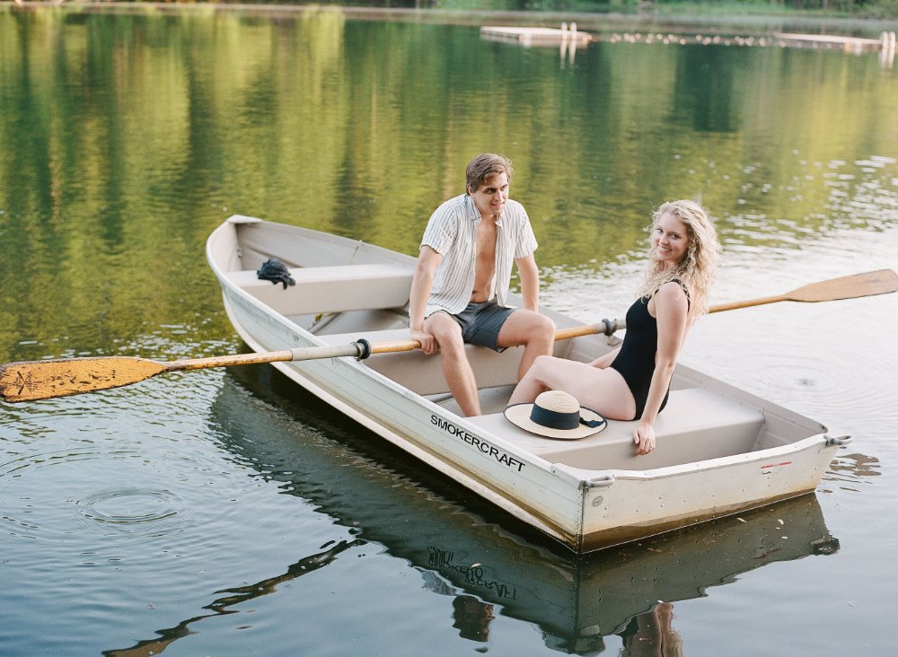  Couple sitting in a rowboat on the lake during a playful and romantic engagement session. 