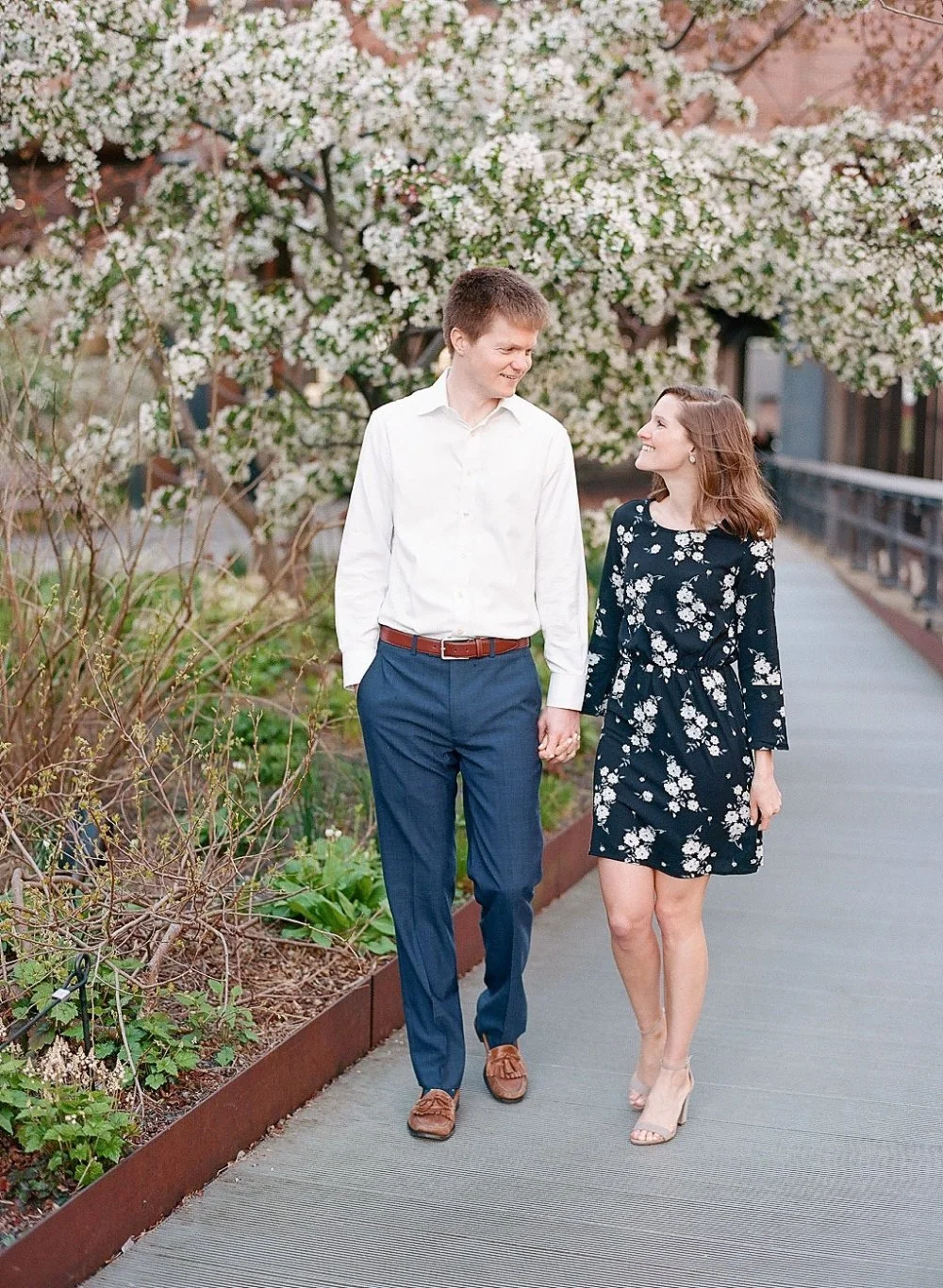  Couple walking through spring blooms in coordinated outfits during a relaxed engagement session. 