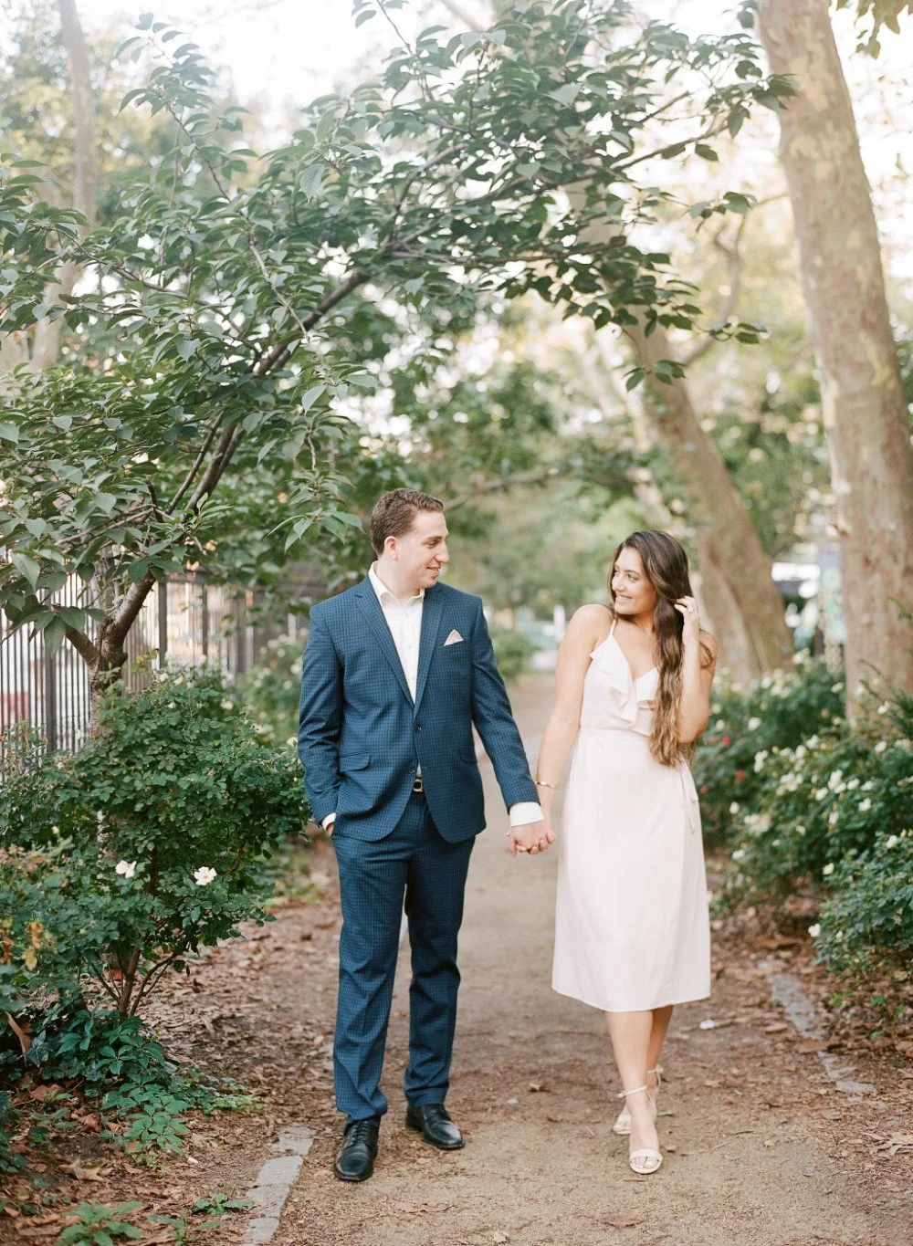  Couple holding hands beneath trees during an elegant outdoor engagement session. 