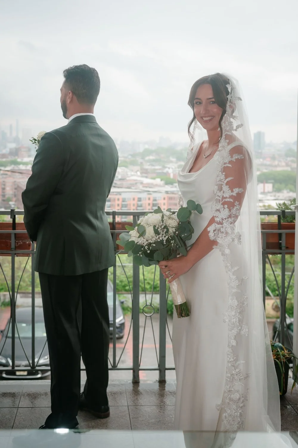  Bride smiling toward the camera before a wedding first look ideas moment with groom waiting nearby. 