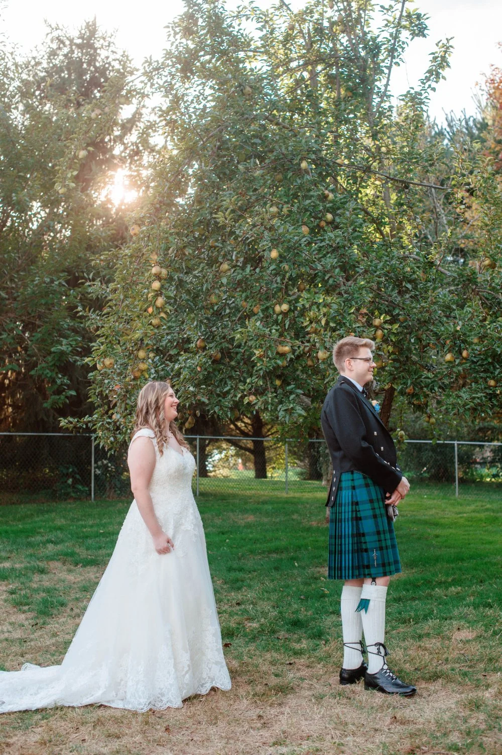  Bride approaching groom during an outdoor wedding first look ideas moment beneath sunlit trees. 