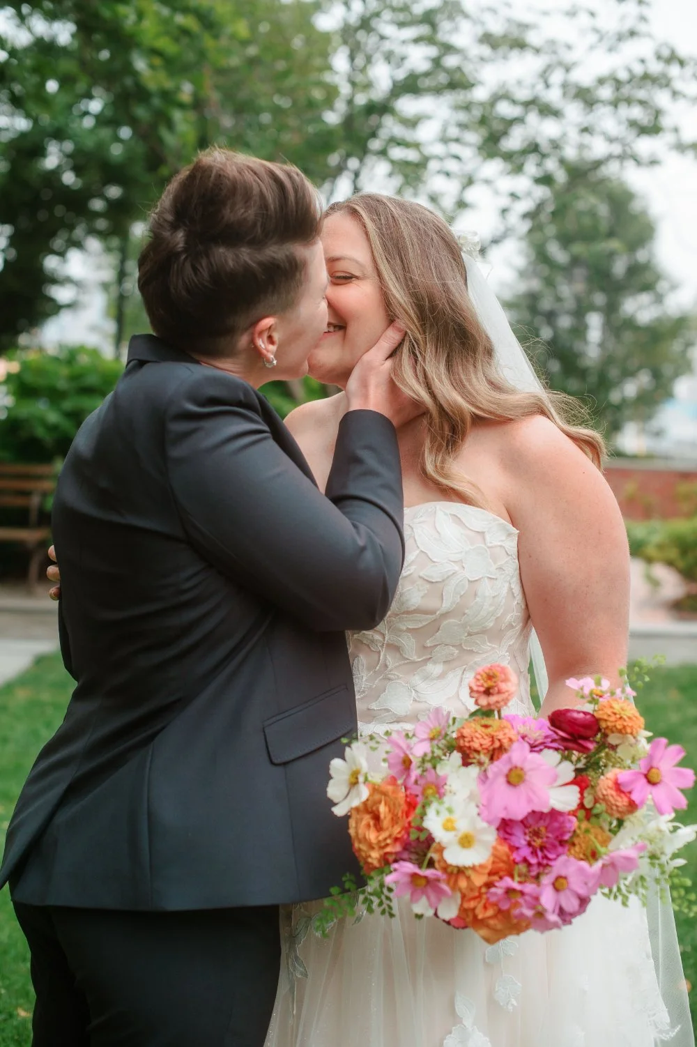  LGBTQ wedding photographer captures newly married couple sharing a kiss while holding colorful wedding bouquets. 