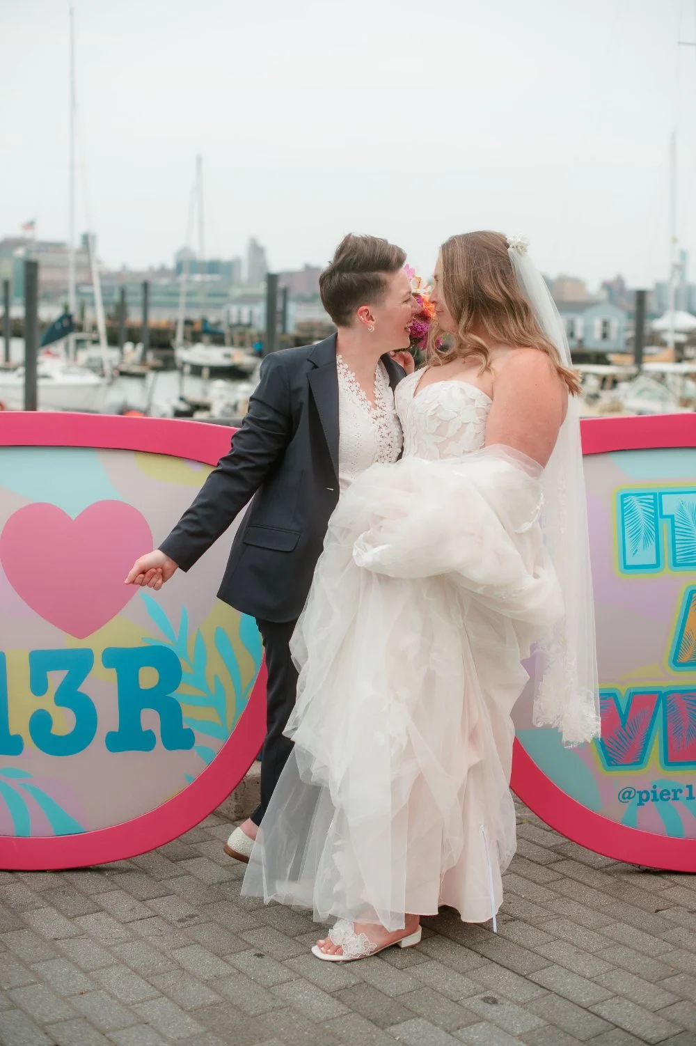  LGBTQ wedding photographer captures newlyweds smiling together by a colorful mural at their waterfront wedding. 