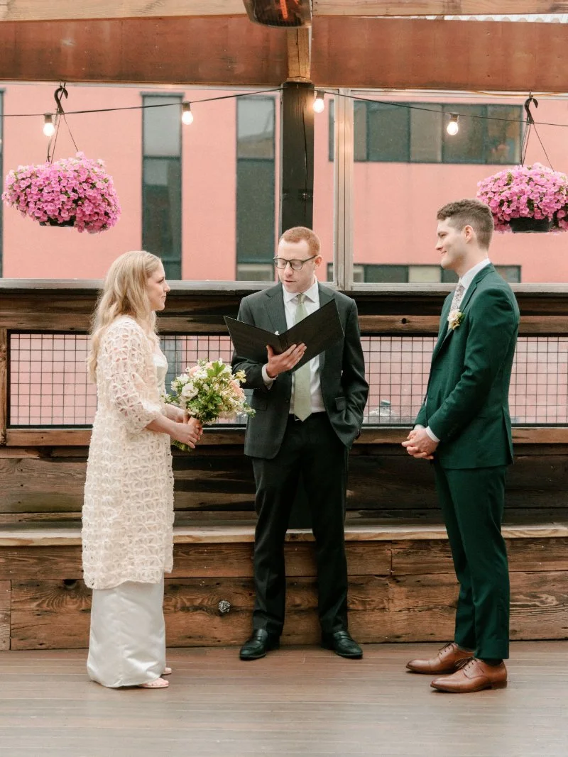   Couple exchanging wedding vows during an intimate rooftop wedding ceremony with their officiant.  