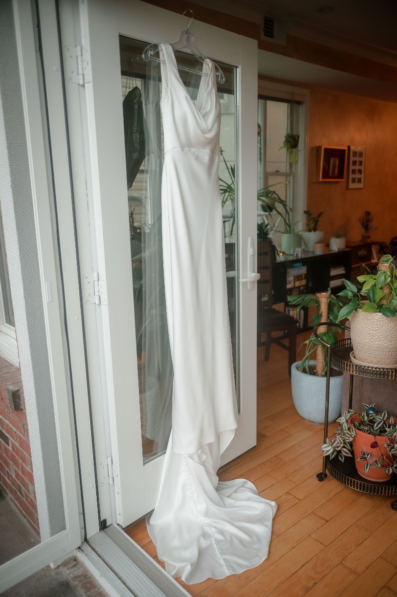  White wedding dress hanging by a glass door, offering inspiration for helpful wedding dress tips. 