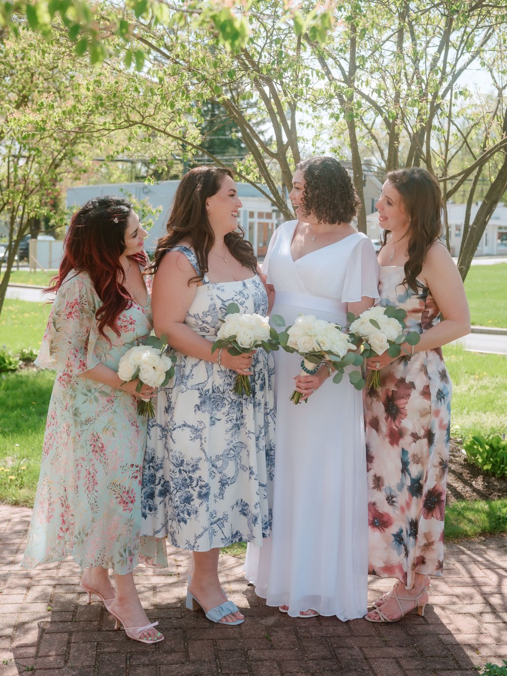  Bride smiling with three loved ones holding bouquets during an outdoor wedding portrait. 