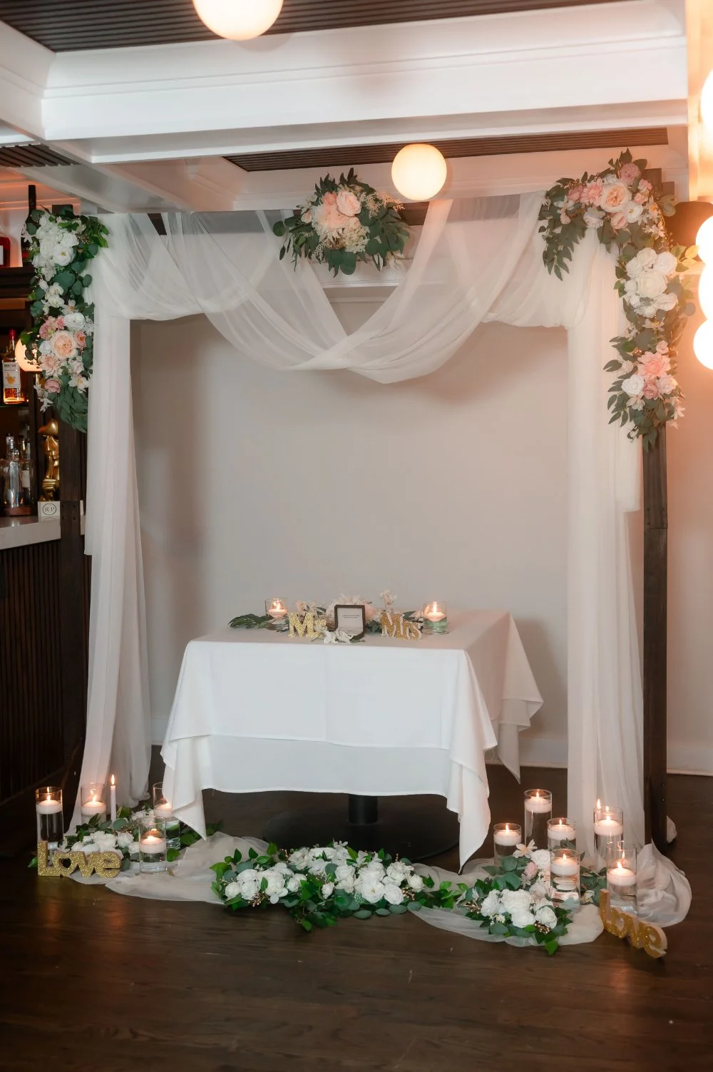  Elegant indoor holiday wedding ceremony setup with white drapery, greenery, soft candlelight, and a decorated table for an intimate NYC or New Jersey wedding. 