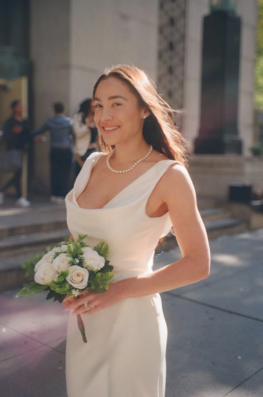  Smiling bride holding a white rose bouquet on a sunny NYC street during her elopement. 