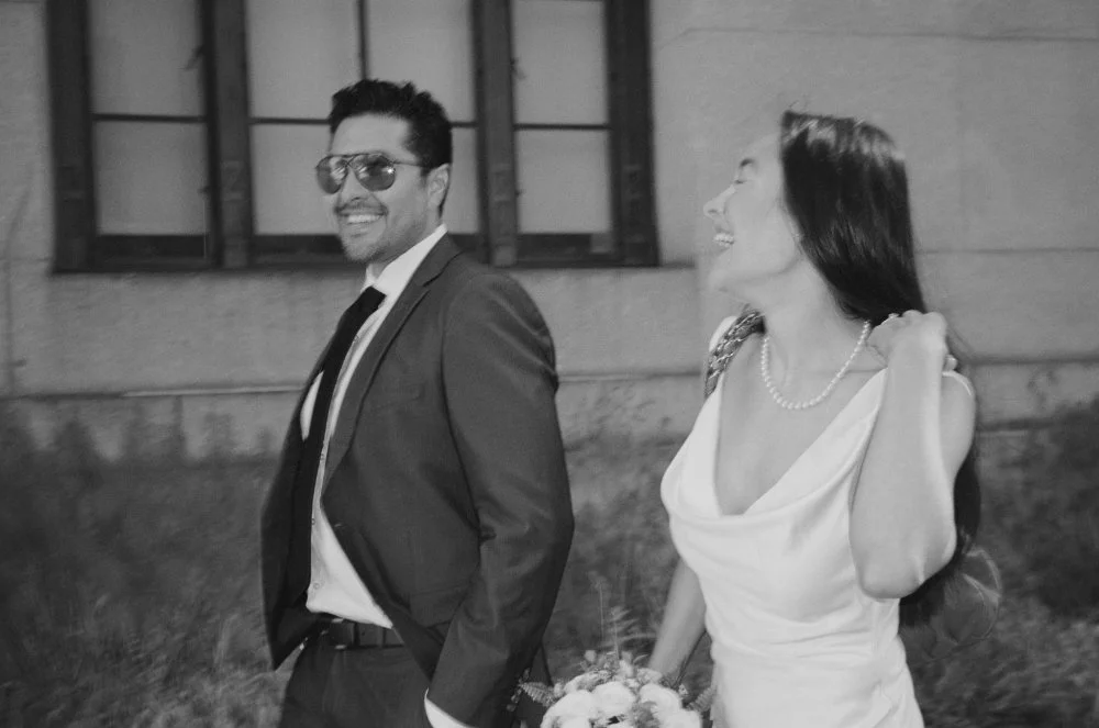  Black and white NYC elopement photo of a couple walking together, smiling in their wedding attire. 