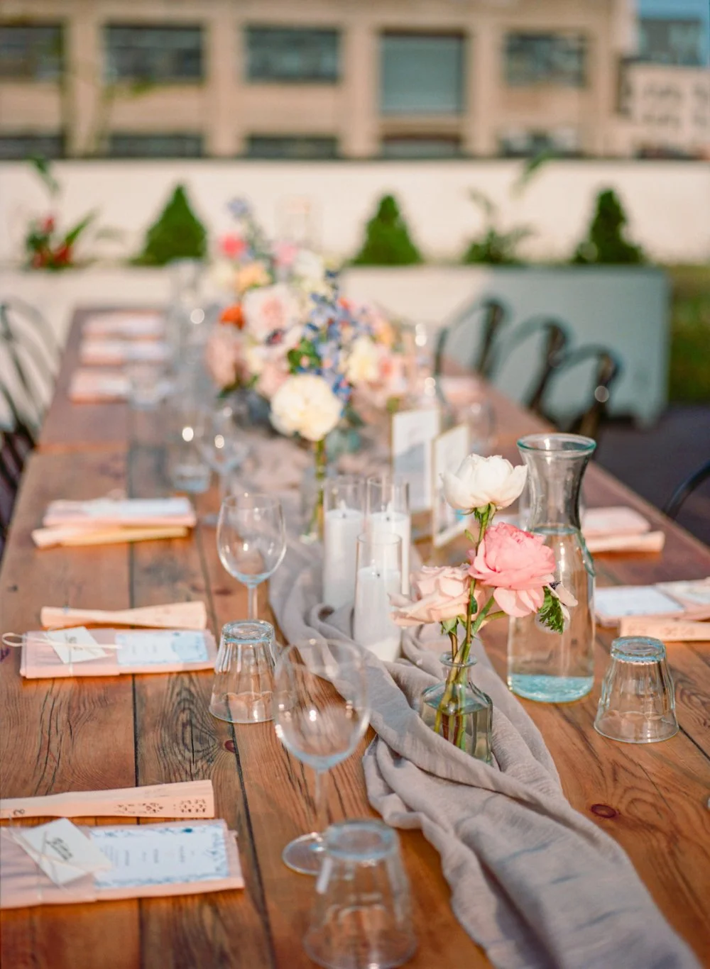 Rustic wedding reception table decorated with pink flowers, candles, glassware, and soft neutral linens.