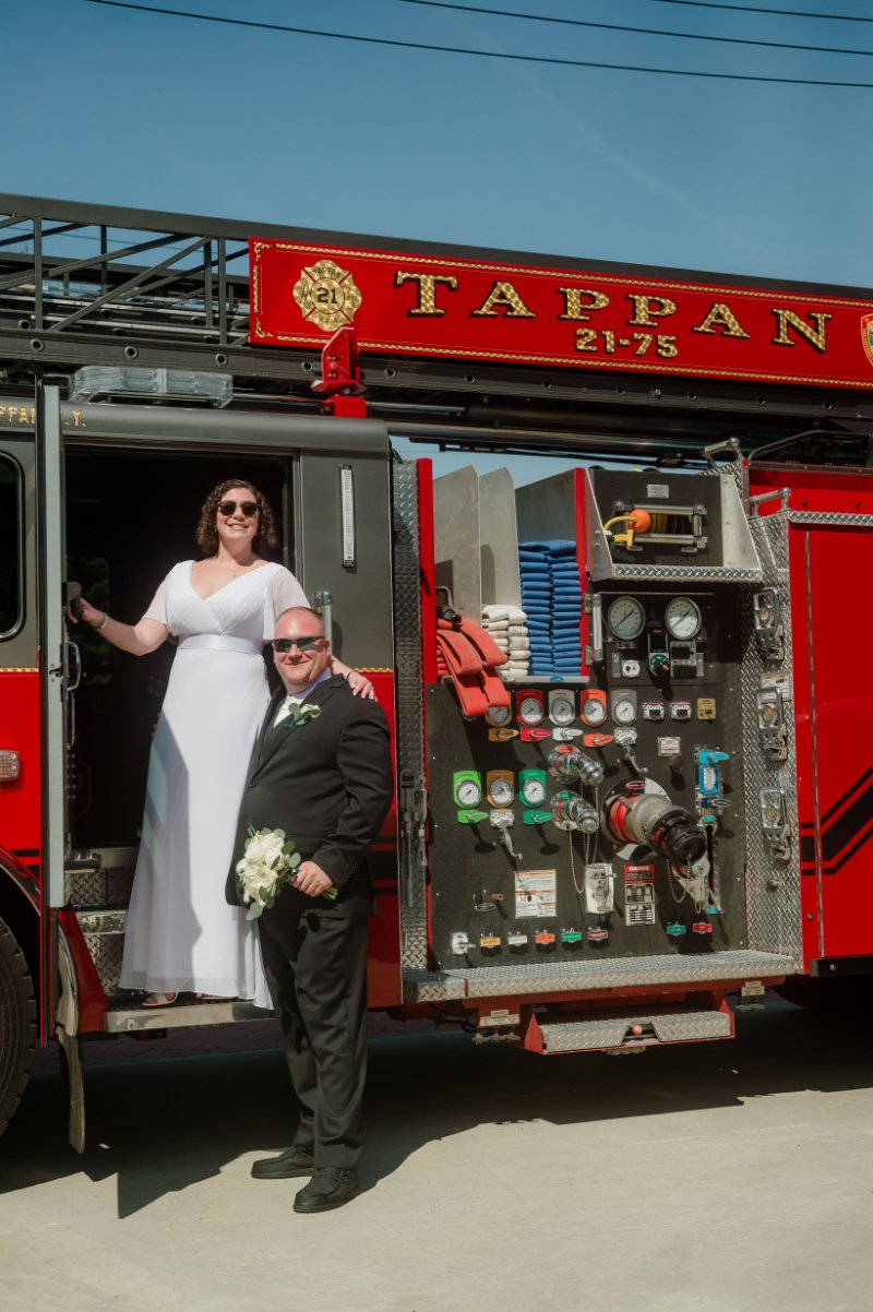 Newlyweds smiling together beside a red Tappan fire truck after their wedding ceremony.