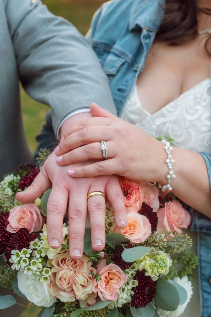Close up of bride and groom hands with wedding rings resting on bouquet before they announce your elopement.