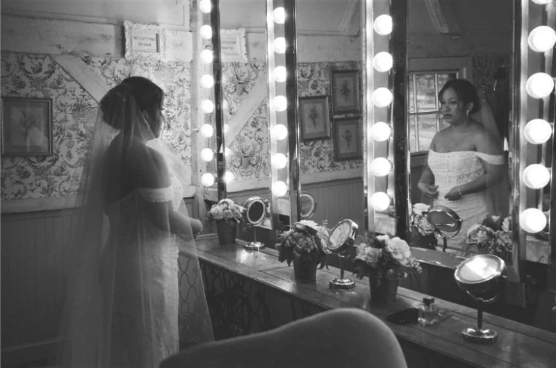 A bride pauses at the vanity mirror, deep in reflection—one of those overlooked wedding moments of calm.