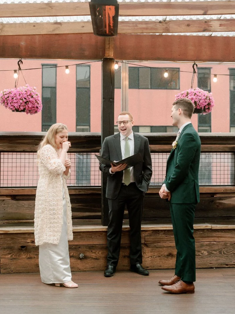 Rooftop wedding ceremony with couple laughing during vows, officiant reading, and relaxed intimate setting
