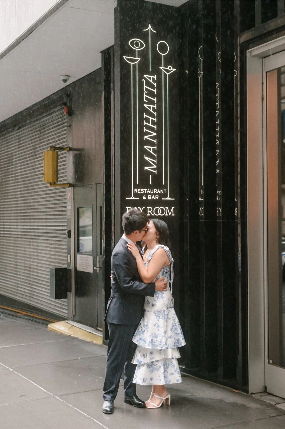 Couple sharing a romantic kiss outside a restaurant during their NYC elopement, with the bride wearing a blue and white floral dress and the groom in a dark suit.