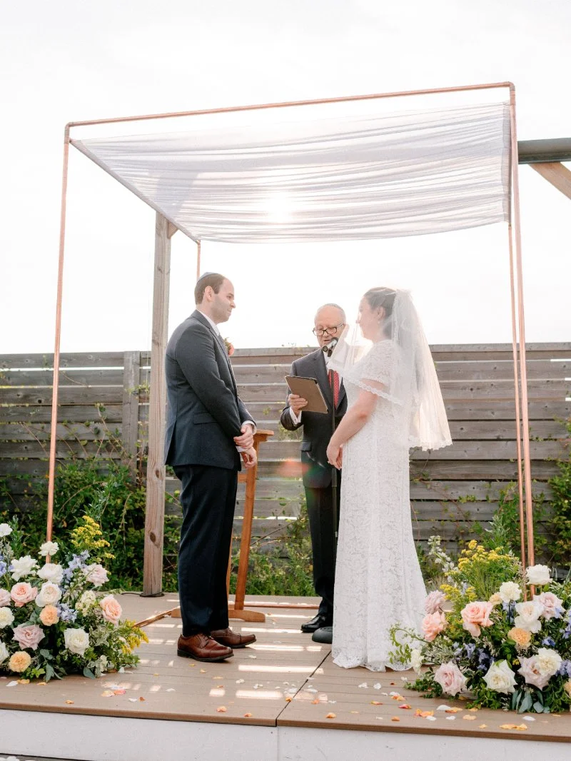 Couple exchanging wedding vows during an intimate outdoor wedding ceremony beneath a simple draped arch.