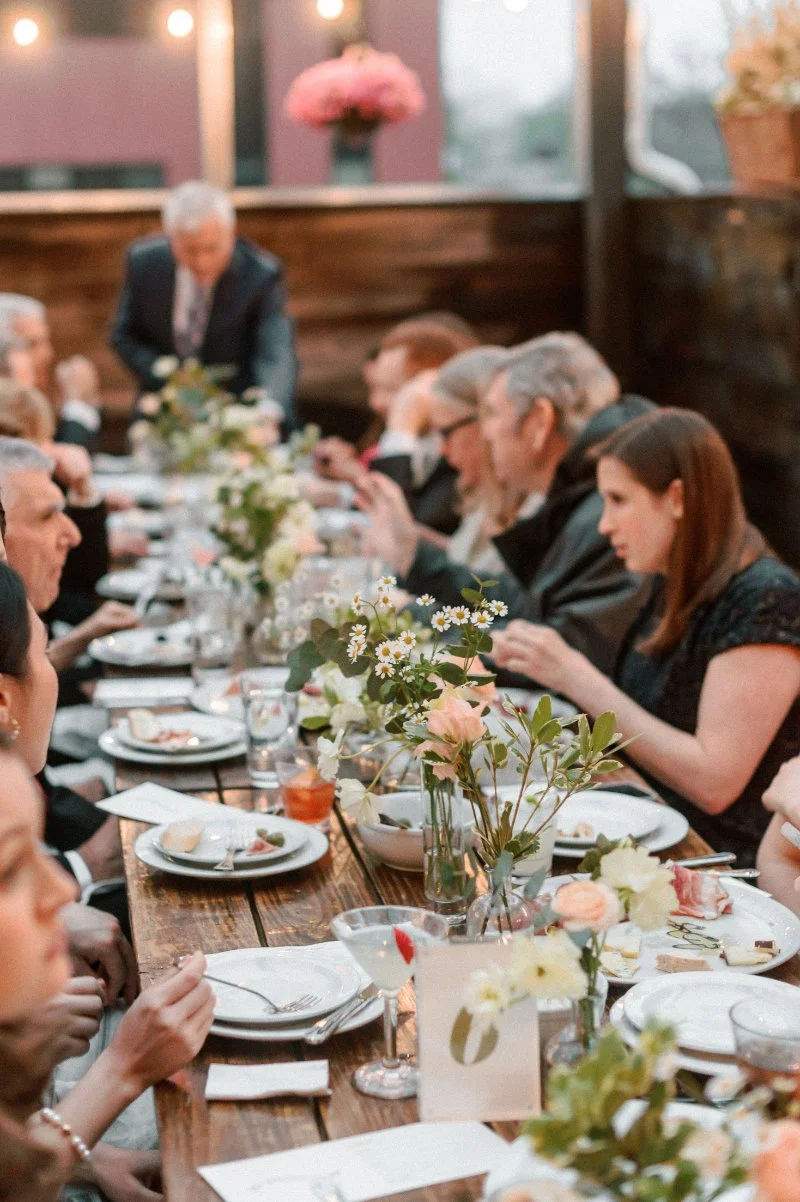 Intimate rooftop wedding dinner with guests, long table, soft florals, and warm evening light