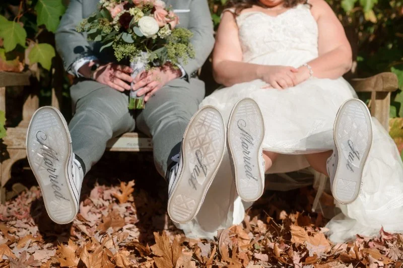 Newlyweds show off “Just Married” sneakers while sitting in autumn leaves after their big wedding exit.