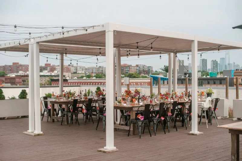 Outdoor rooftop reception setup for intimate celebration with long wooden tables, colorful florals, and support from a wedding planner for a small wedding.