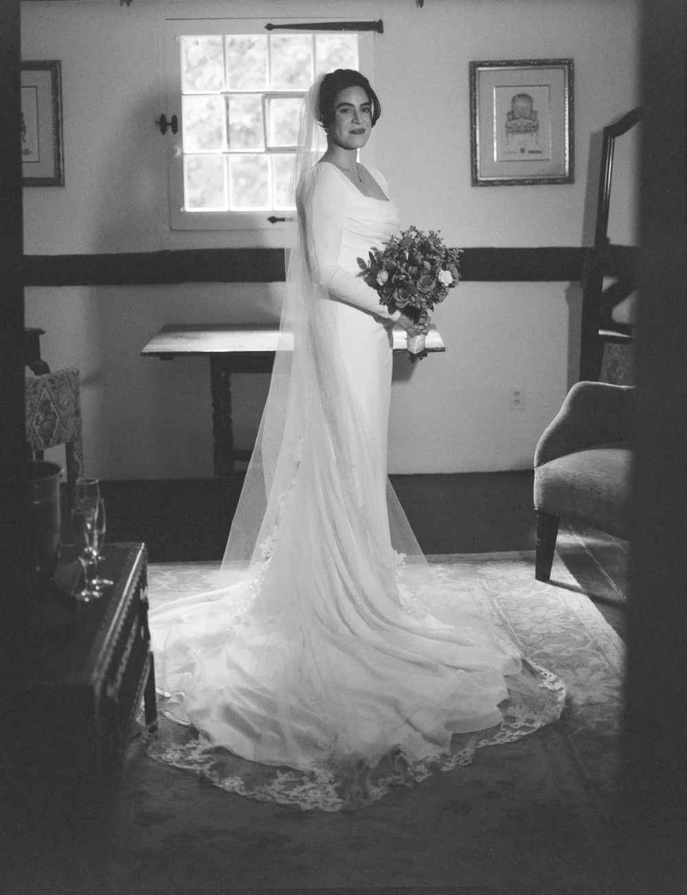 Black-and-white portrait of a bride in a long-sleeved wedding dress holding a floral bouquet.