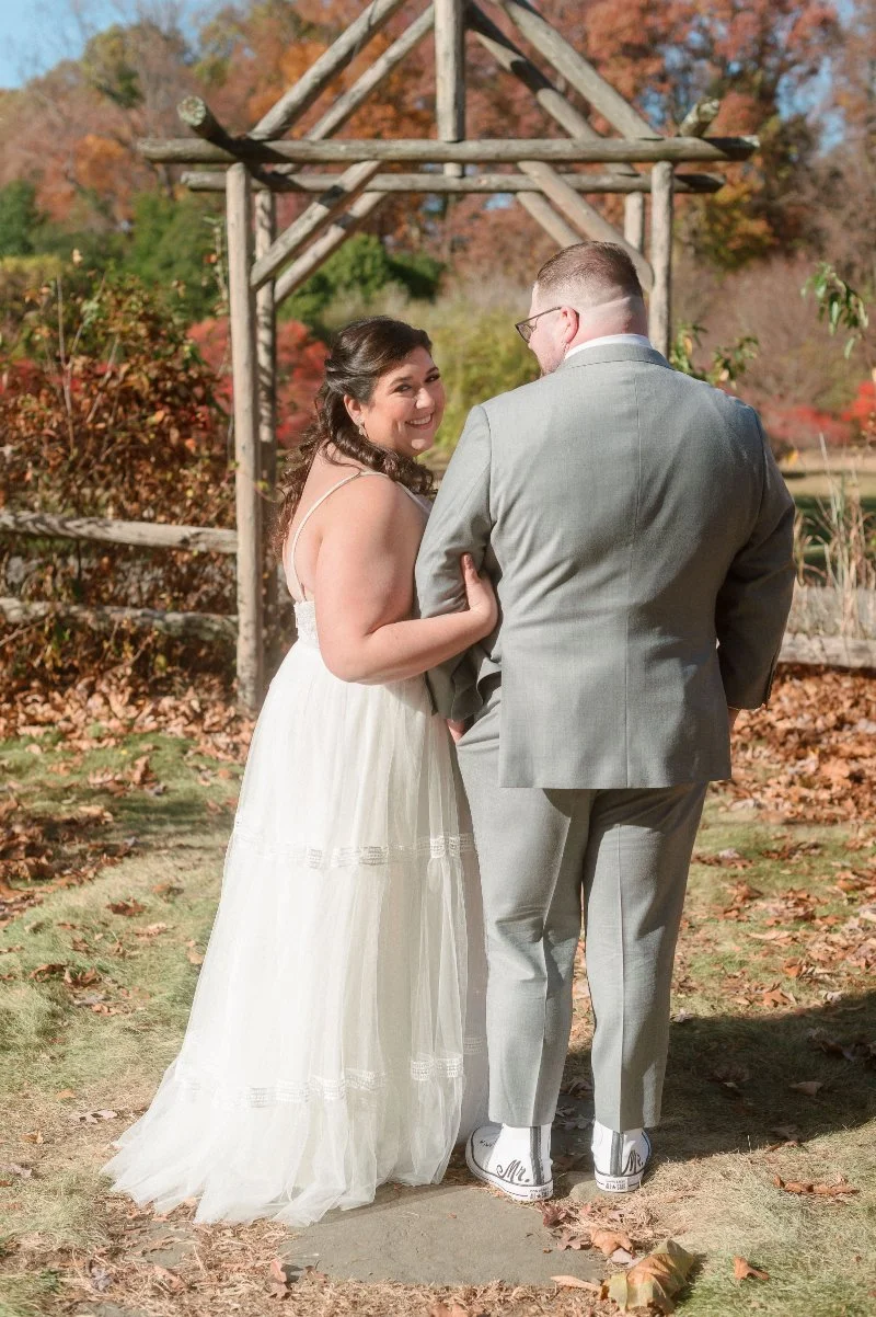 Bride smiling at camera while walking with groom through autumn garden after they announce your elopement.