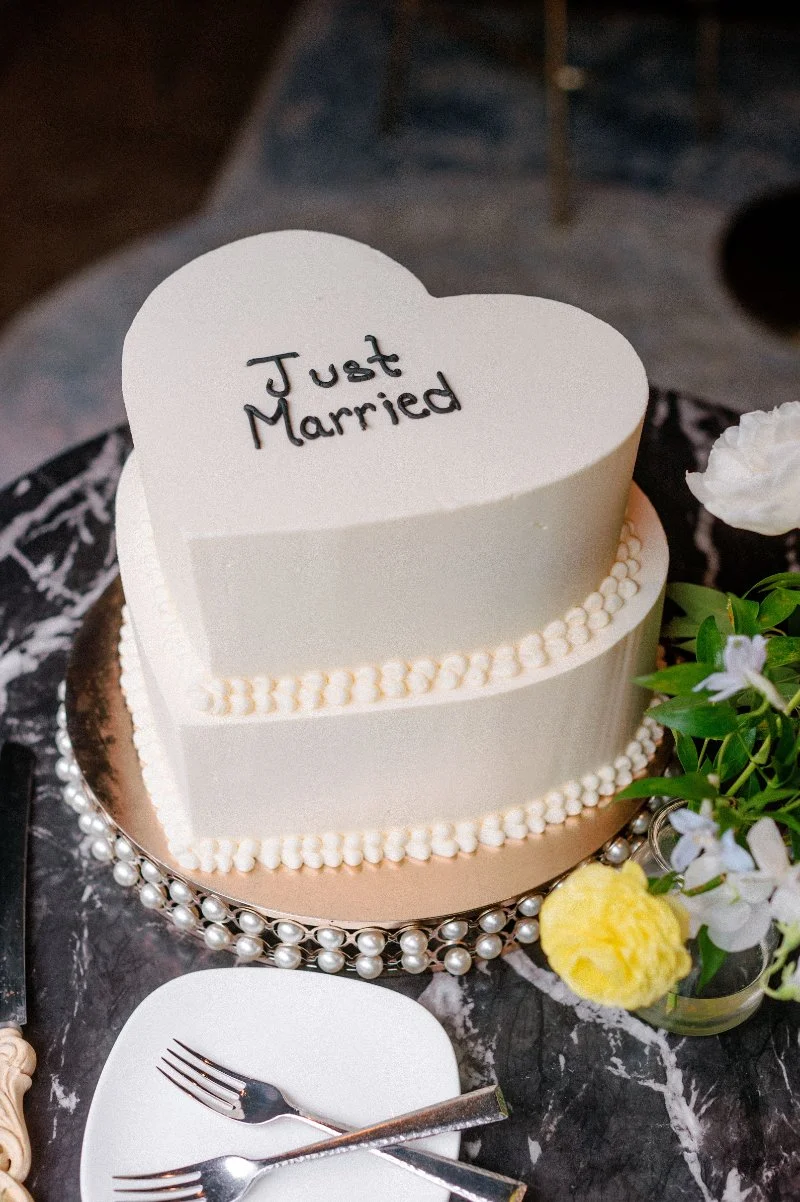 Heart-shaped wedding cake with “Just Married” detail, soft white frosting, and delicate floral accents