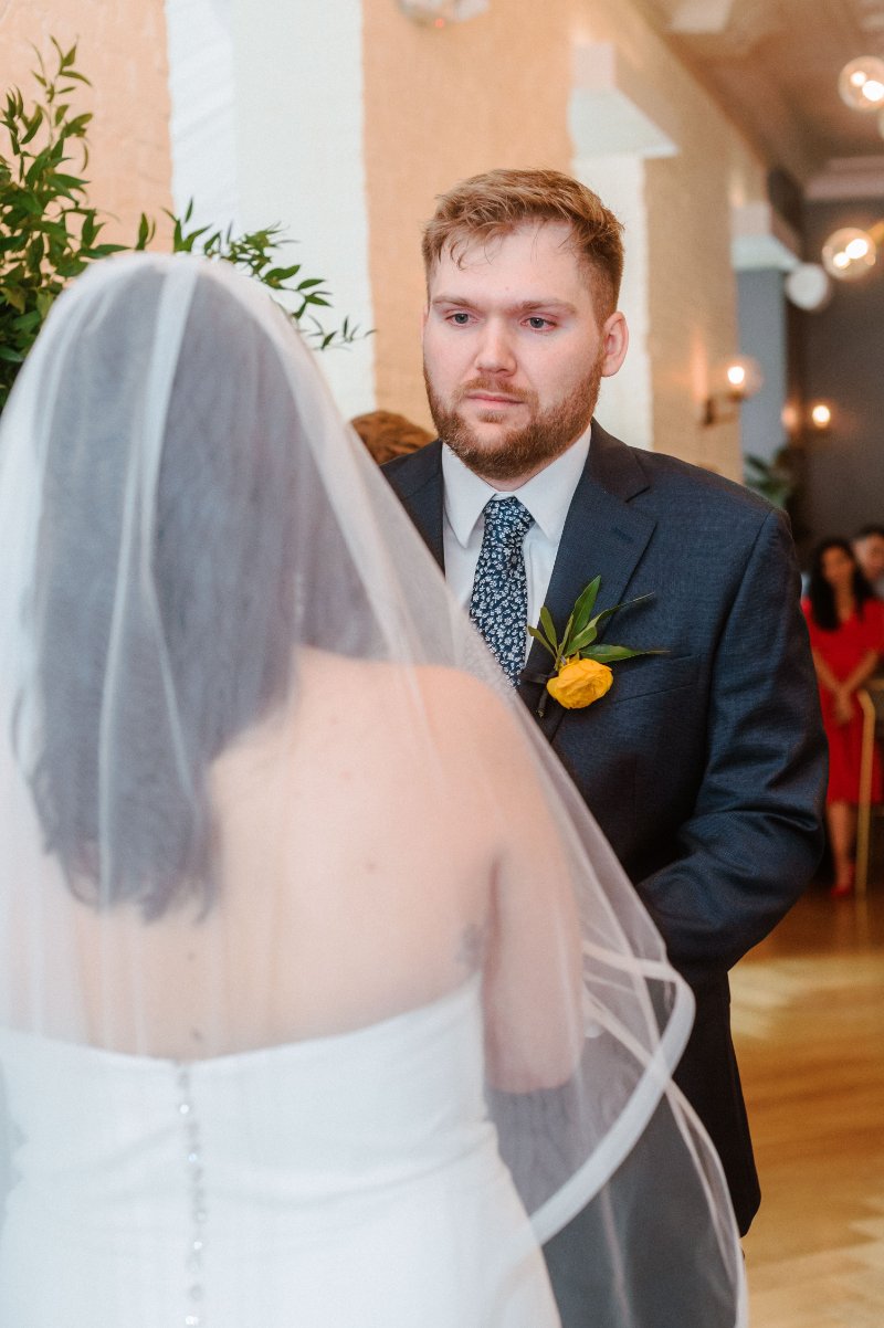Groom looking at his bride during an emotional indoor wedding ceremony.