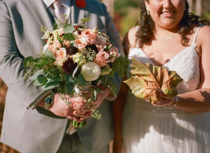 Couple holding bouquet and autumn leaf during outdoor ceremony before they announce your elopement.