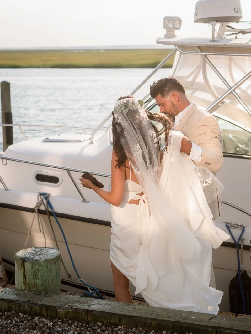 Bride and groom boarding a boat together, with her veil flowing in the waterfront breeze.