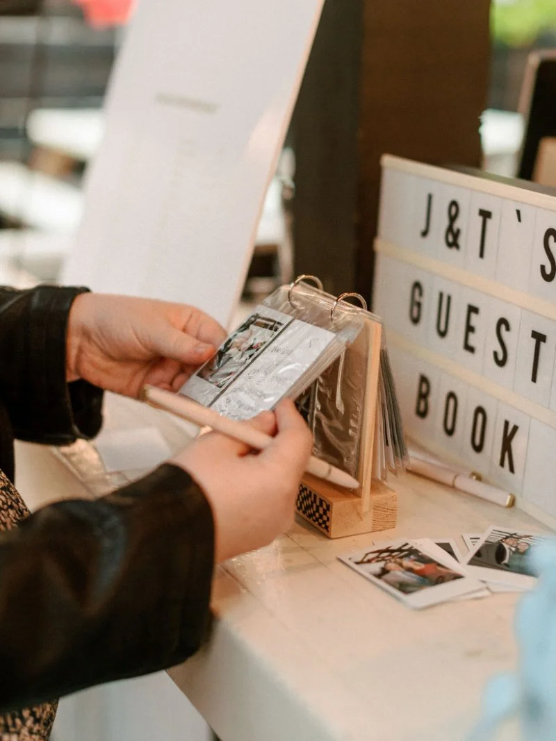 Wedding guest flipping through photo guest book display at intimate reception, thoughtfully arranged by a wedding planner for a small wedding.