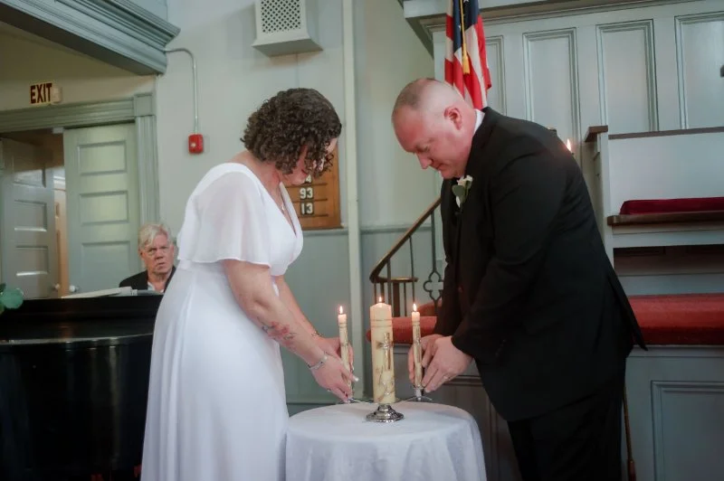 Newlyweds lighting a unity candle together during their intimate church wedding ceremony.