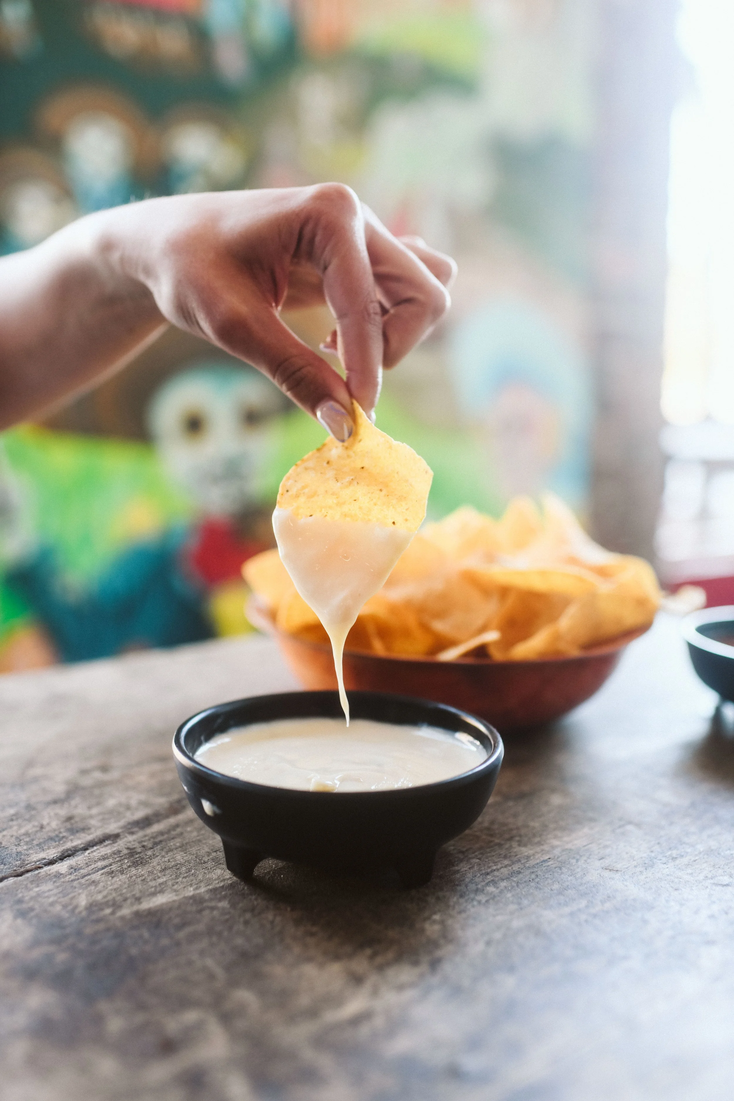 A tortilla chip being dipped into queso sauce at Howling Wolf Taqueria